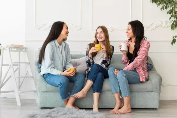 women-sitting-sofa-chatting-holding-cups-hand